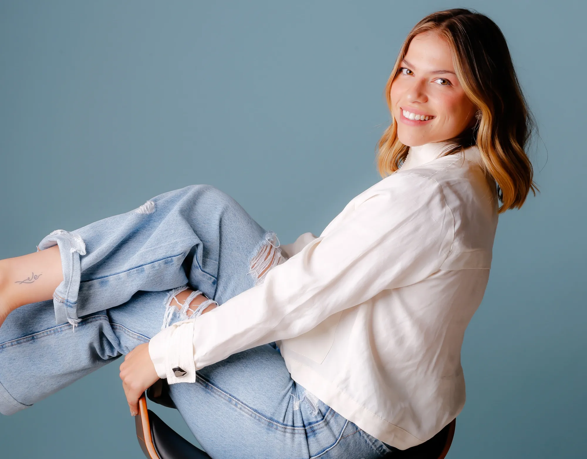 Mulher de camisa branca e jeans sentada sorrindo